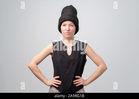 Young serious confident woman in black hat and clothes posing on a gray background Stock Photo