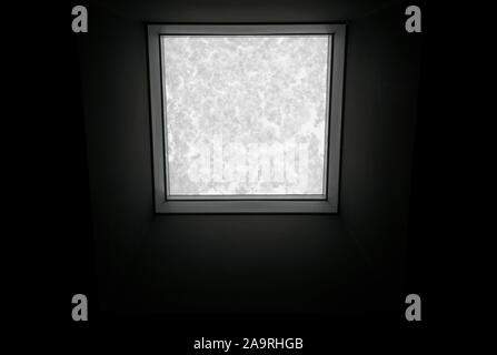 View through the roof window covered by melted snow from inside the building on the black background. Stock Photo