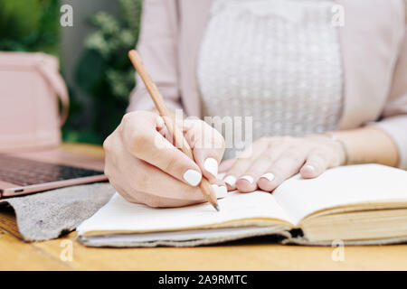 Manicured hands of female student taking notes in planner and writing down her schedule Stock Photo