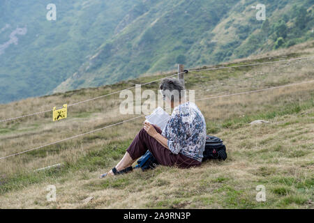 Ticino, Switzerland - August 5, 2019: Old lady read magazine with cigarette on top of Monte Tamaro Stock Photo