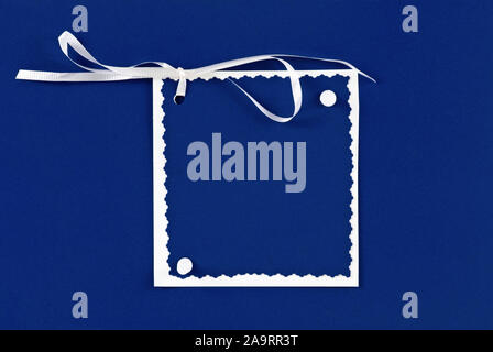Unique homemade blank Christmas gift card in blue and white. Each piece of paper is on top of the next larger size paper. A white ribbon is attached. Stock Photo