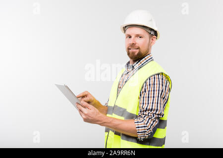 Young successful builder in white hardhat, checkered shirt and yellow vest Stock Photo