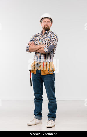 Young successful bearded repairman in white hardhat, jeans and checkered shirt Stock Photo