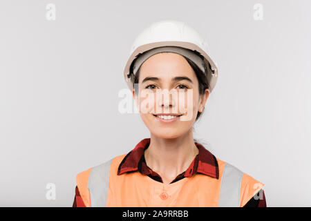 Pretty young smiling female builder in hardhat and working vest looking at you Stock Photo