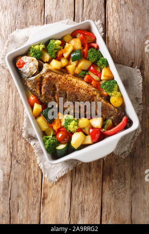 River fish baked carp with vegetables close-up in a baking dish on the table. Vertical top view from above Stock Photo