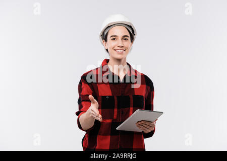 Happy young female architect in hardhat and flannel welcoming you by handshake Stock Photo