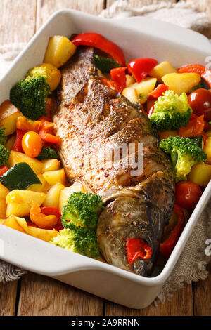 Baked carp with vegetables close-up in a baking dish on the table. vertical Stock Photo