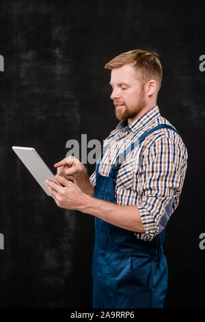Young successful bearded technician in workwear pointing at touchpad screen Stock Photo