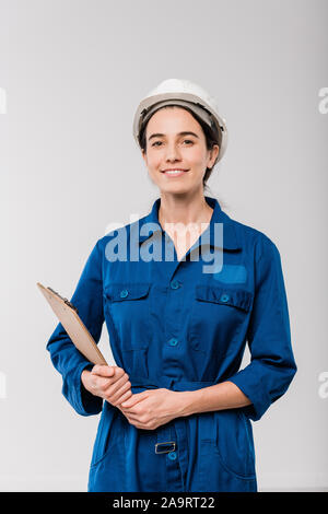 Happy young female mechanic in blue workwear and hardhat holding clipboard Stock Photo