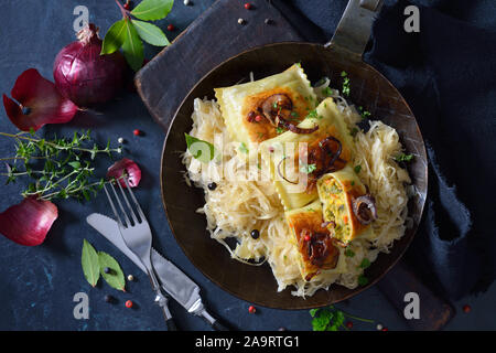 Fried Swabian vegetable ravioli with roasted onions and sauerkraut served in an iron frying pan Stock Photo