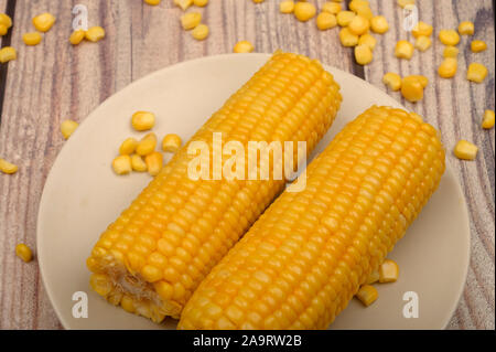 Two ears of boiled corn in a plate and a grain of corn on the table. Healthy diet. Fitness diet. For a sweet treat. Close up Stock Photo