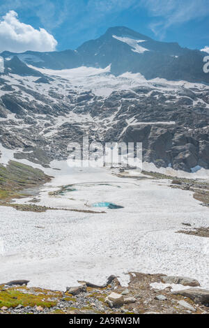 Turquoise lake created by melting ice and snow at the feet of an alpine glacier. Frozen, icy pond in the snow. Italian Alps during melting season. Stock Photo