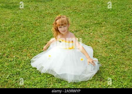 Little girl in a yellow festive dress on a green lawn Stock Photo