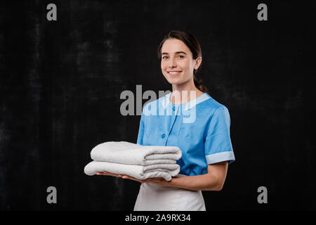 Pretty young chamber maid in uniform holding two folded white soft towels Stock Photo