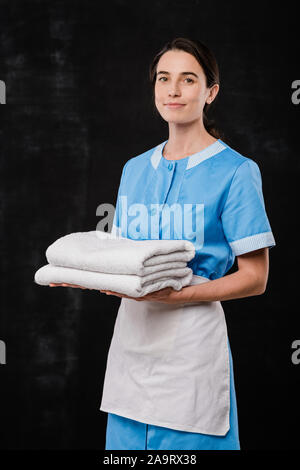 Pretty young brunette chamber maid in uniform holding two folded soft towels Stock Photo