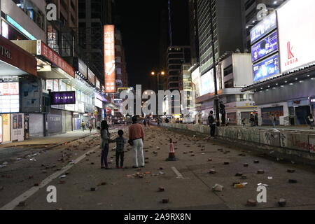 Hong Kong, China. 17th Nov 2019. A family of onlookers gaze silently at the streets of Mong Kok, an area that is typically bustling with shoppers and tourists, but is now covered with bricks intended to block incoming police and traffic. Moments later, police fire tear gas towards the direction of the family, causing them to flee in panic. The near-daily use of tear gas has been linked to increasing health concerns as mysterious skin conditions in children and journalists have suddenly appeared. Credit: Katherine Cheng/Alamy Live News Stock Photo