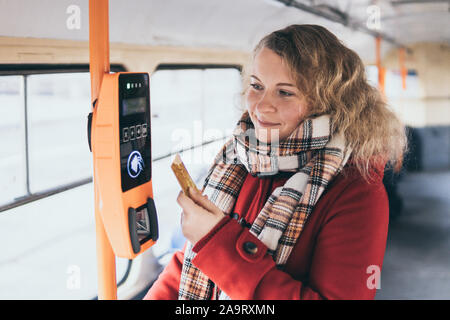 Young blonde Caucasian woman making cashless payment of public transport ticket fare at automatic contactless machine with a card Stock Photo