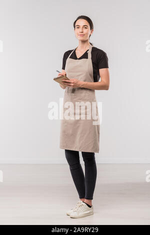 A cute young waiter in a white T-shirt and a blue apron holding a cup ...