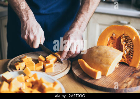 Man cuts orange pumpkin in the kitchen at home Stock Photo