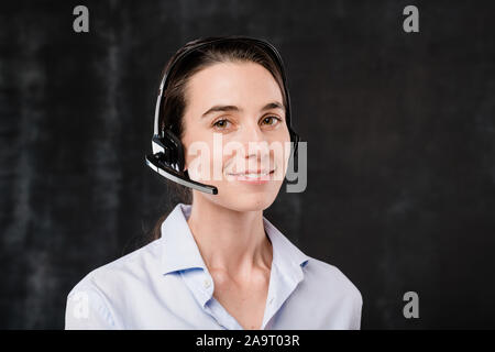 Pretty young brunette operator with headset talking to clients during work Stock Photo