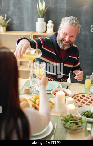 Happy mature man pouring orange juice into glass of his daughter by dinner Stock Photo