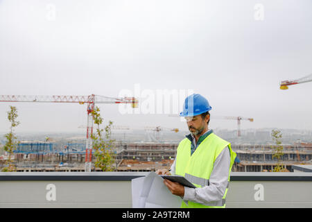 Architect working on a building site with the electronic tablet and plans Stock Photo