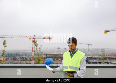 Architect working on a building site with the electronic tablet and plans Stock Photo