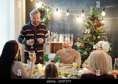 Bearded mature man with glass of wine toasting in front of his family by dinner Stock Photo