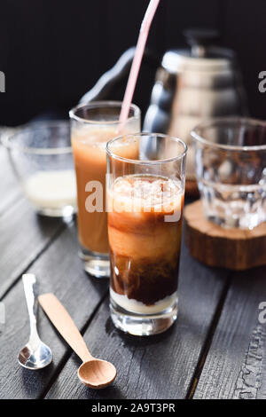 Iced layered coffee with coconut milk in tall glasses on black background closeup Stock Photo