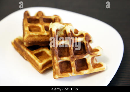 Belgian waffles in a white plate on dark wooden table. Healthy breakfast, pieces of freshly baked classic wafer Stock Photo