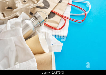 Zero waste concept. Eco friendly reusable items in natural shopping bag. Paper bag, coffee cups and metal bottle on blue background Stock Photo