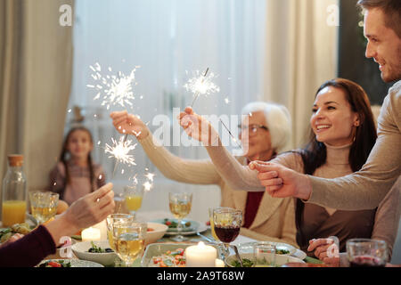 Cheerful young and mature adults holding sparkling bengal lights by xmas dinner Stock Photo