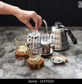 Making pour over Vietnamese milk coffee. Woman hand pressing coffee in phin on dark background copy space Stock Photo