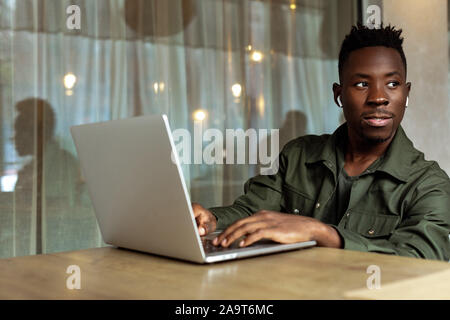 Cheerful young african american man in headphones using computer in cafe Stock Photo