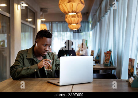 Cheerful young african american man in headphones using computer in cafe Stock Photo