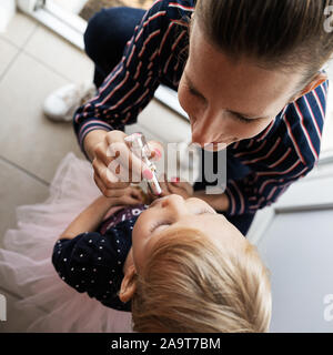 View from above of a happy fashionable young mother putting lipstick on her toddler daughter. Stock Photo