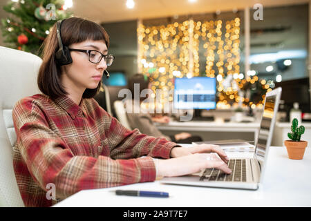 Young serious female operator typing on laptop keypad while organizing work Stock Photo