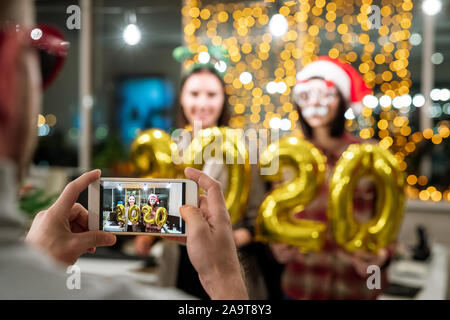 Hands of man holding smartphone with two young happy businesswomen on screen Stock Photo