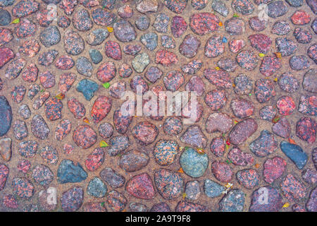 Stone background of pavement with rough wet granite boulders. Texture of historic medieval cobble paving is laid on the city street Stock Photo