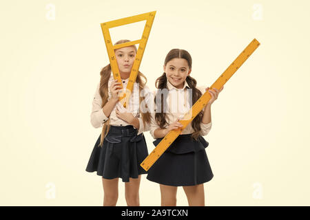 Our favorite lesson. Little girls preparing for geometry lesson. Cute schoolgirls holding triangular and ruler for lesson. Small children with measuring instruments at school lesson. Stock Photo