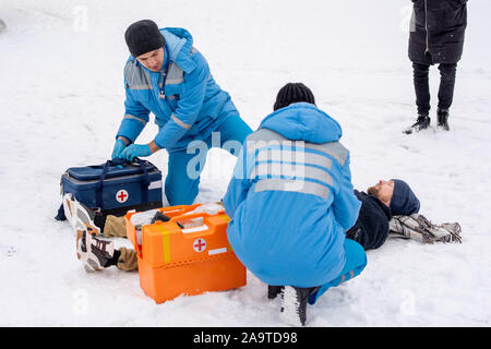 Two paramedics in uniform giving first aid to sick unconscious man lying on snow Stock Photo