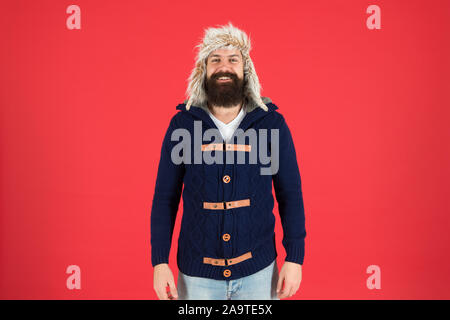 Fashion menswear shop. Masculine clothes concept. Winter menswear. Clothes design. Man bearded stand warm jumper and hat on red background. Winter season menswear. Hipster rustic style furry hat. Stock Photo