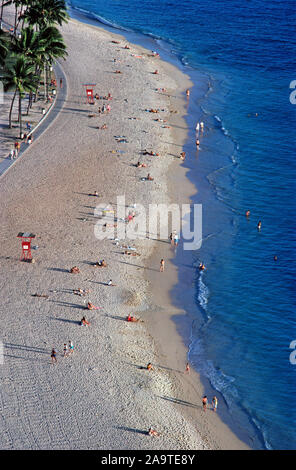 The crowds of sunbathers thin out as the sun sets on the white sands of famous Waikiki Beach, a popular destination for vacationers who come to the capital city of Honolulu on Oahu, one of the eight major islands in the Pacific Ocean that are part of the tropical state of Hawaii, USA. This aerial photograph shows only a small part of Waikiki Beach, which is two miles (3.2 kilometers) long and actually has eight sections with individual beach names. Most populated are the sands and walking promenades in front of historic and high-rise hotels along the meandering shoreline. Stock Photo