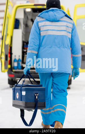 Rear view of paramedic in blue workwear and gloves carrying first aid kit Stock Photo