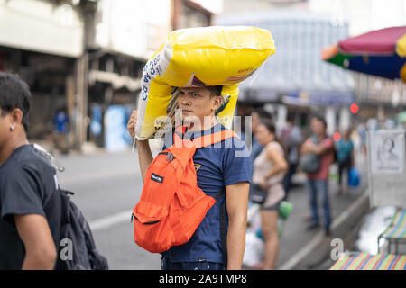 A young Filipino man balances a 50kg bag of rice on his head whilst waiting for public transportation. Stock Photo