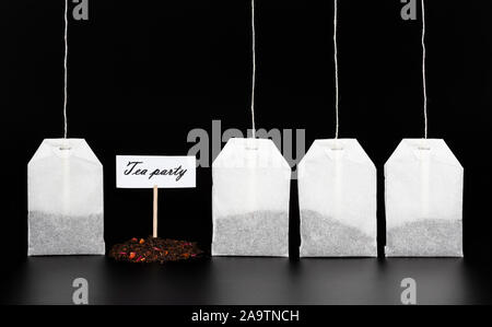 Four tea bags and a slide of dry tea with the sign "Tea Party" on a dark background. The concept of tea drinking, tea ceremony. Stock Photo