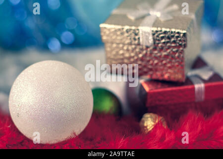 Christmas gift card with a big white ball in the foreground and gift boxes in the background. Red, gold and blue colors. Very shallow focus on the bal Stock Photo