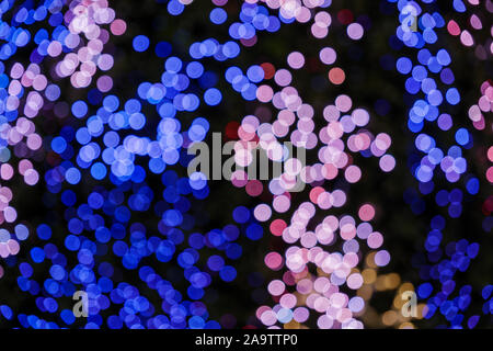 Illuminated abstract round red, purple, blue and magenta bokeh on dark background. Colourful glitter bokeh from out of focus view of decoration bulbs. Stock Photo