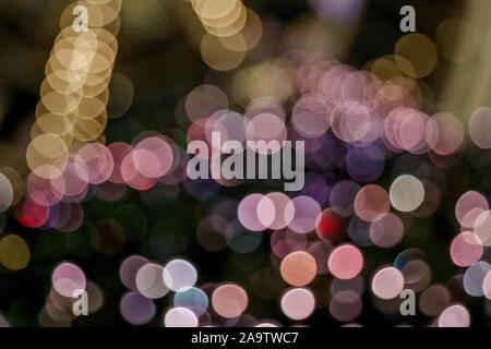 Illuminated abstract round pink, yellow purple and gold bokeh on dark background. Colourful glitter bokeh from out of focus view of decoration bulbs. Stock Photo