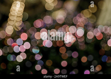 Illuminated abstract round pink, yellow purple and gold bokeh on dark background. Colourful glitter bokeh from out of focus view of decoration bulbs. Stock Photo